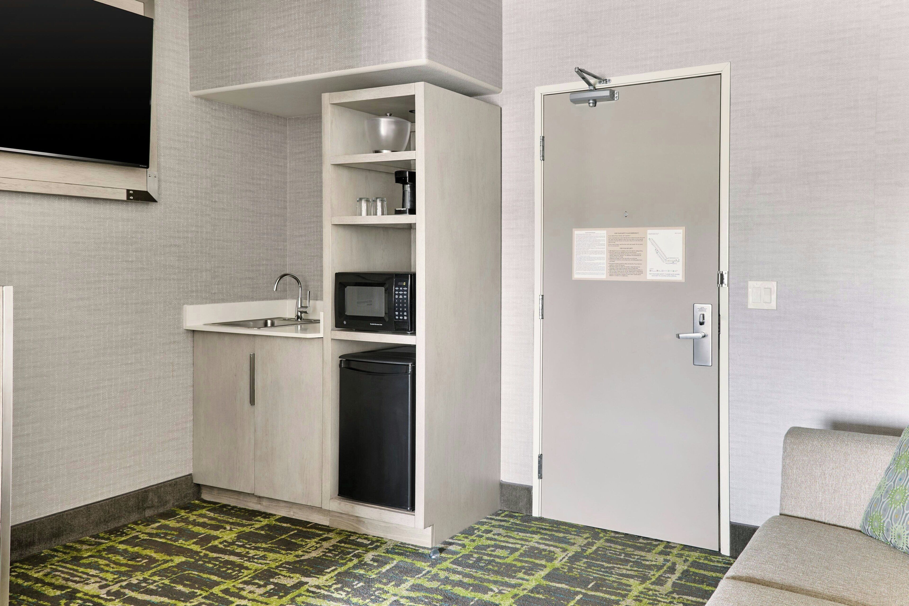 A compact kitchenette with a microwave, sink, and storage cabinets.