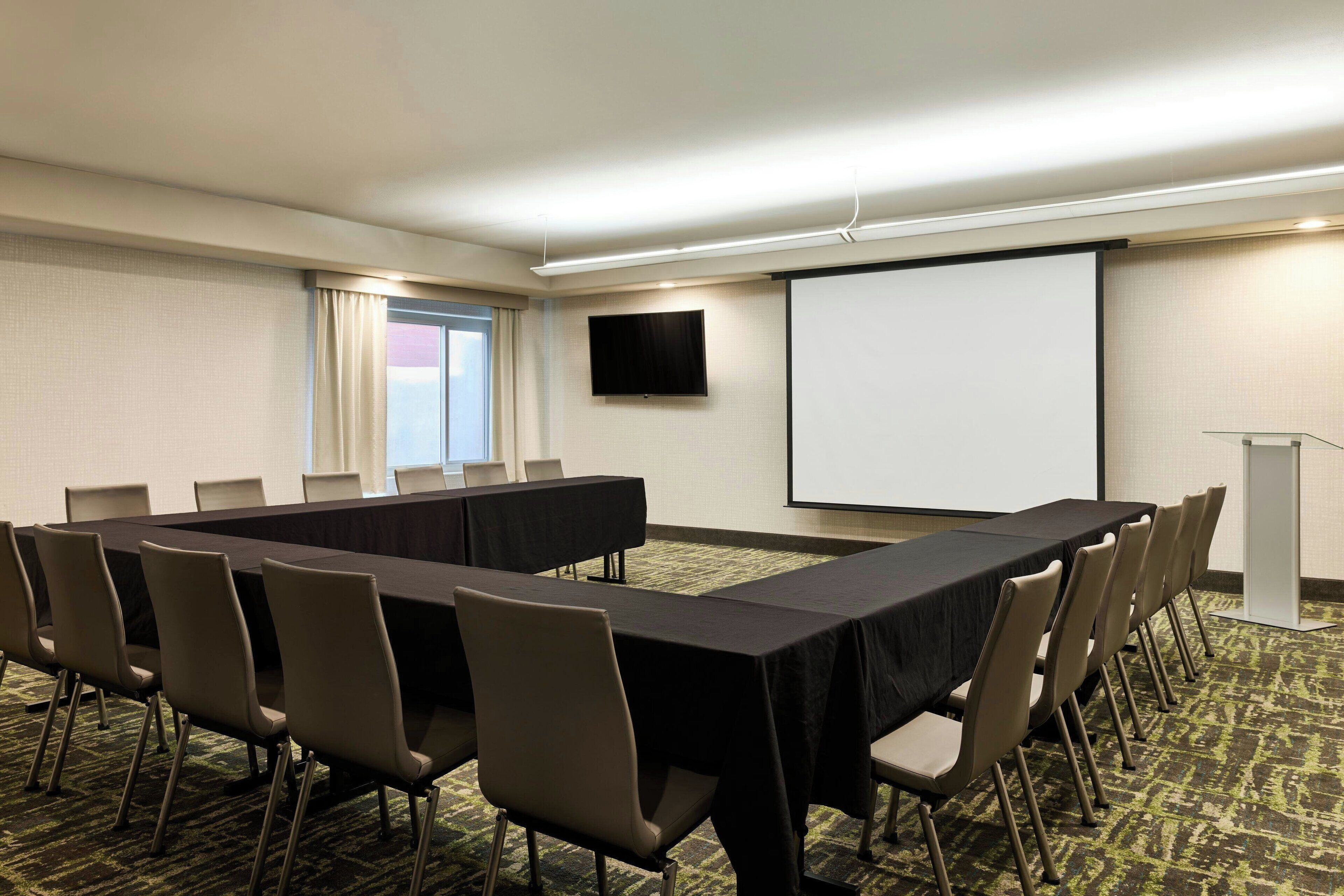 A conference room with a long table, chairs, a projector screen, and a screen for presentations.