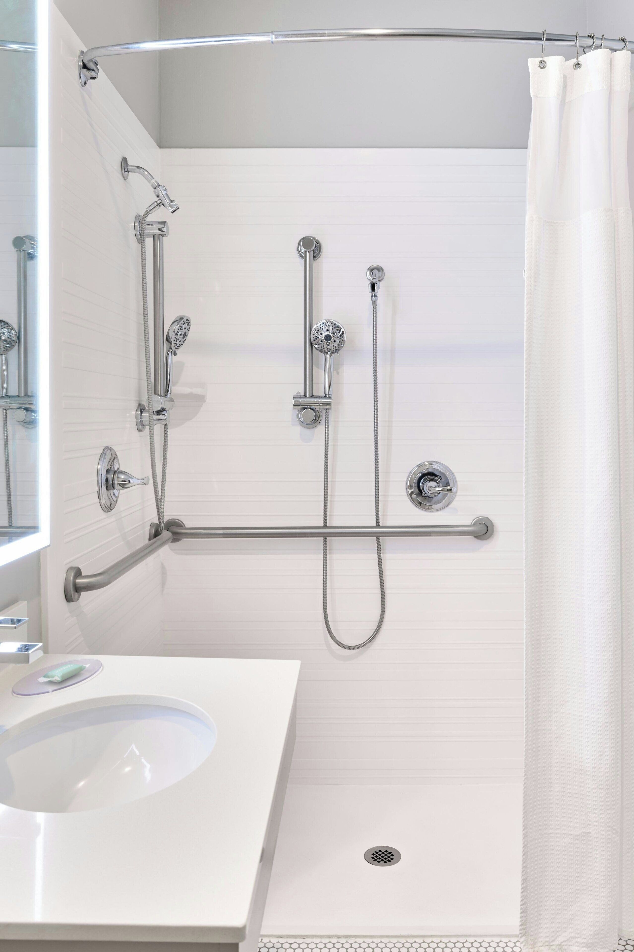 Un baño moderno con un lavamanos blanco, ducha con cerramiento de vidrio y barra de apoyo.