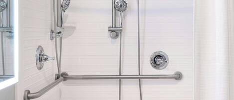 Une salle de bain moderne avec un lavabo blanc, une douche en verre et une barre d’appui.