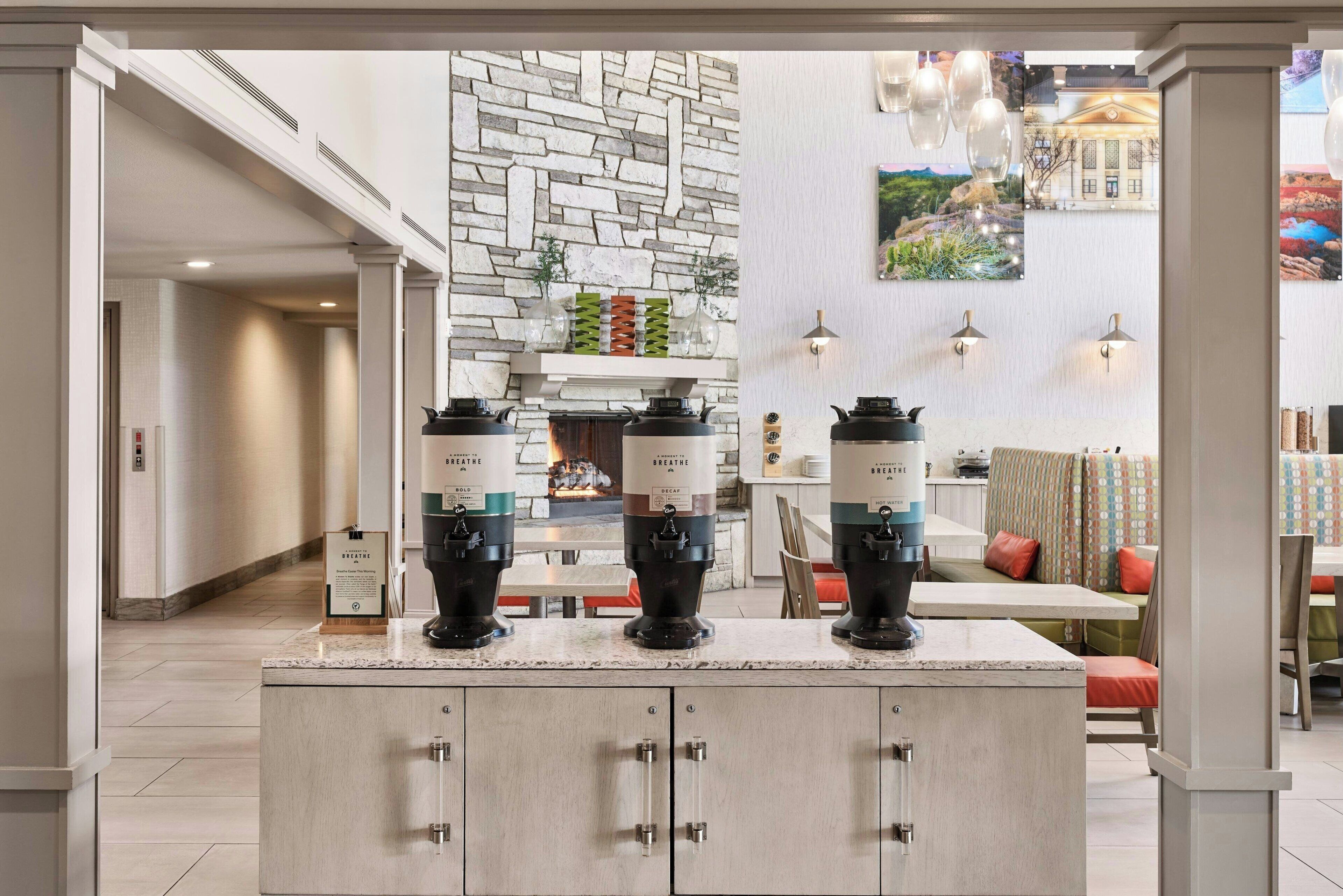 Une cuisine moderne avec un mur en pierres apparentes derrière l’évier, une cuisinière encastrée et trois machines à café posées sur le plan de travail.