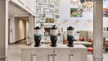 Une cuisine moderne avec un mur en pierres apparentes derrière l’évier, une cuisinière encastrée et trois machines à café posées sur le plan de travail.