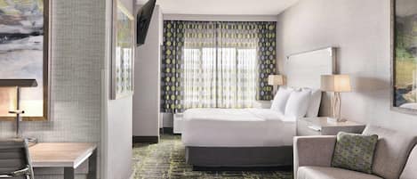 A hotel room with a bed, a desk, a chair, a sofa, and a TV mounted on the wall.
