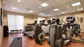 A gym with various exercise equipment, a treadmill, elliptical machines, and a black mat on the floor.
