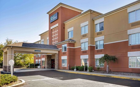 A Stay America hotel with a brick facade, a covered entrance, and a sign indicating the name.