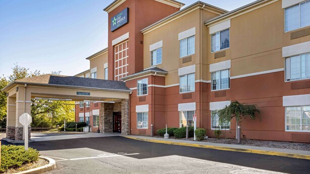Un hotel Stay America con fachada de ladrillo, un acceso cubierto y un cartel con el nombre.
