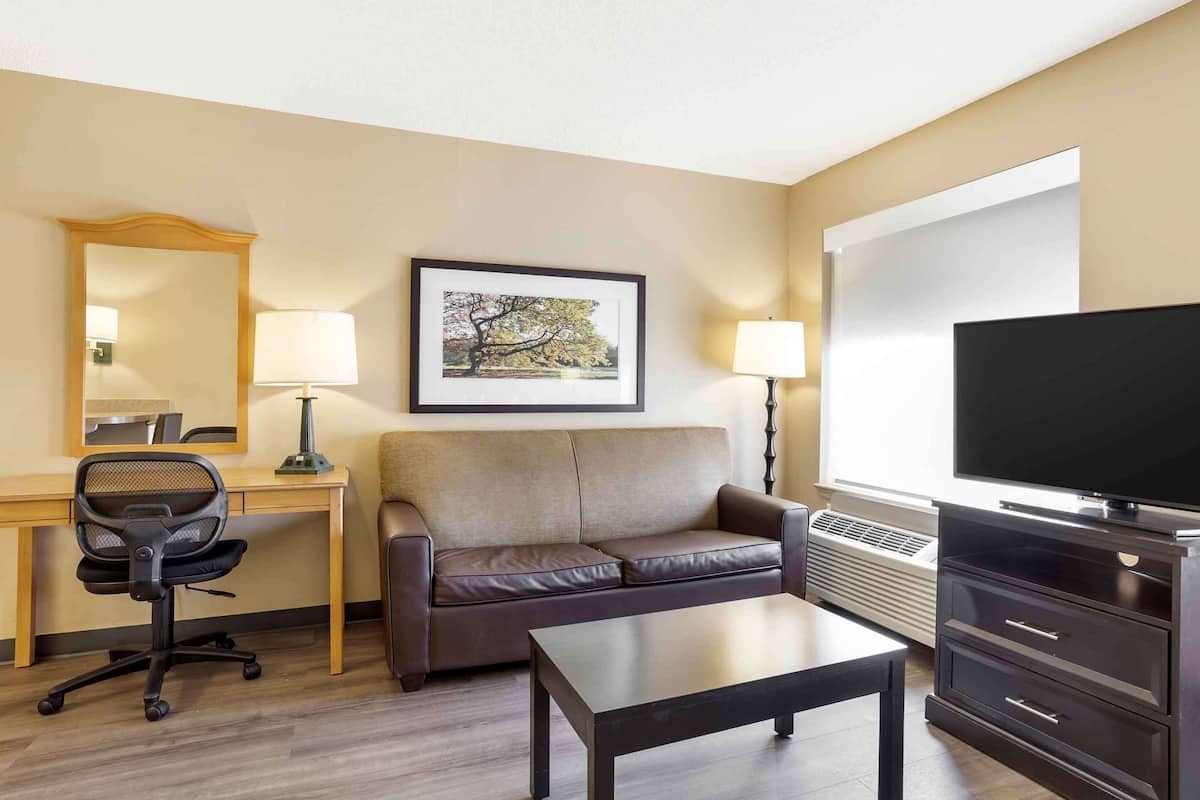 A hotel room with a wooden desk, a leather sofa, a flat-screen TV, a coffee table, and a framed picture on the wall.