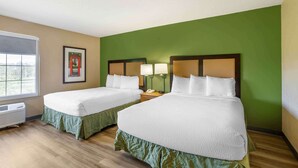 Habitación de hotel con dos camas, paredes verdes, un cuadro enmarcado, lámparas de noche y una ventana con vistas.