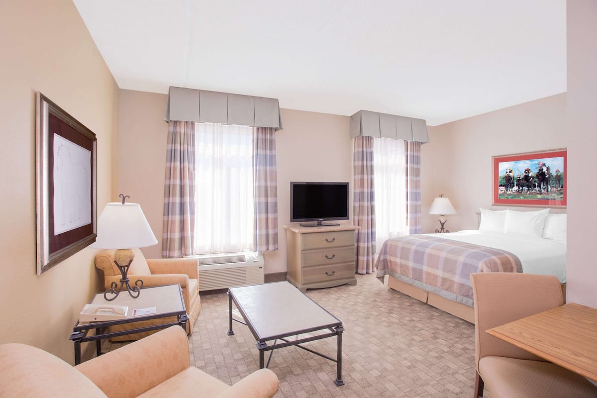 Quarto de hotel com cama, duas poltronas, uma mesinha, televisão e cômoda.