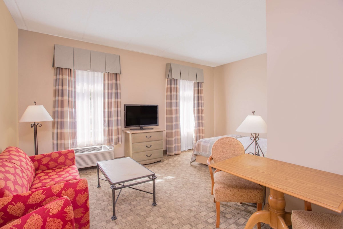 Quarto de hotel com sofá, televisão, escrivaninha, cadeira e cama.