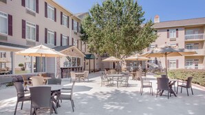 An outdoor patio area with tables and chairs, surrounded by buildings with balconies and windows. - Hawthorn Extended Stay by Wyndham Conyers (Conyers)