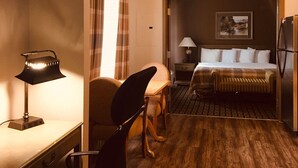 A hotel room with a bed, a desk with a lamp, a chair, a small table, and a refrigerator. - Hawthorn Extended Stay by Wyndham Conyers (Conyers)