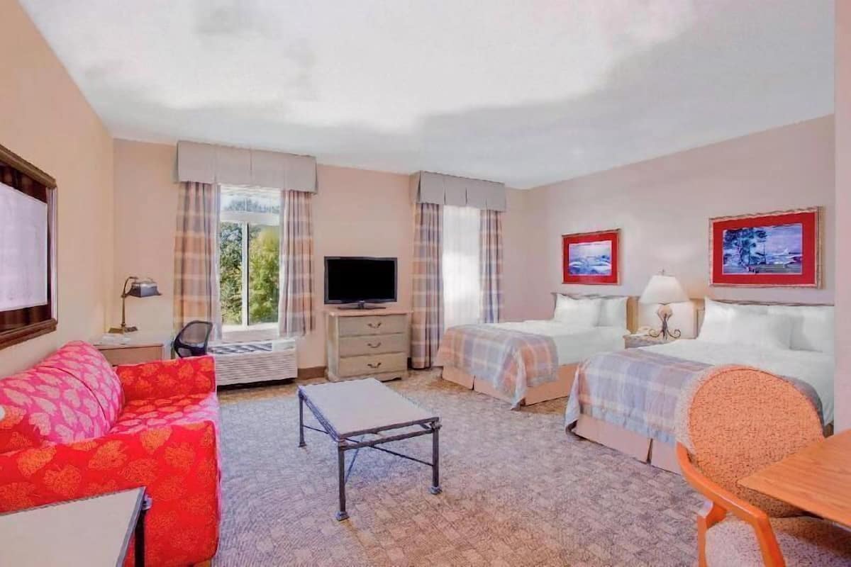 Quarto de hotel com cama, televisão, escrivaninha, cadeira e sofá.