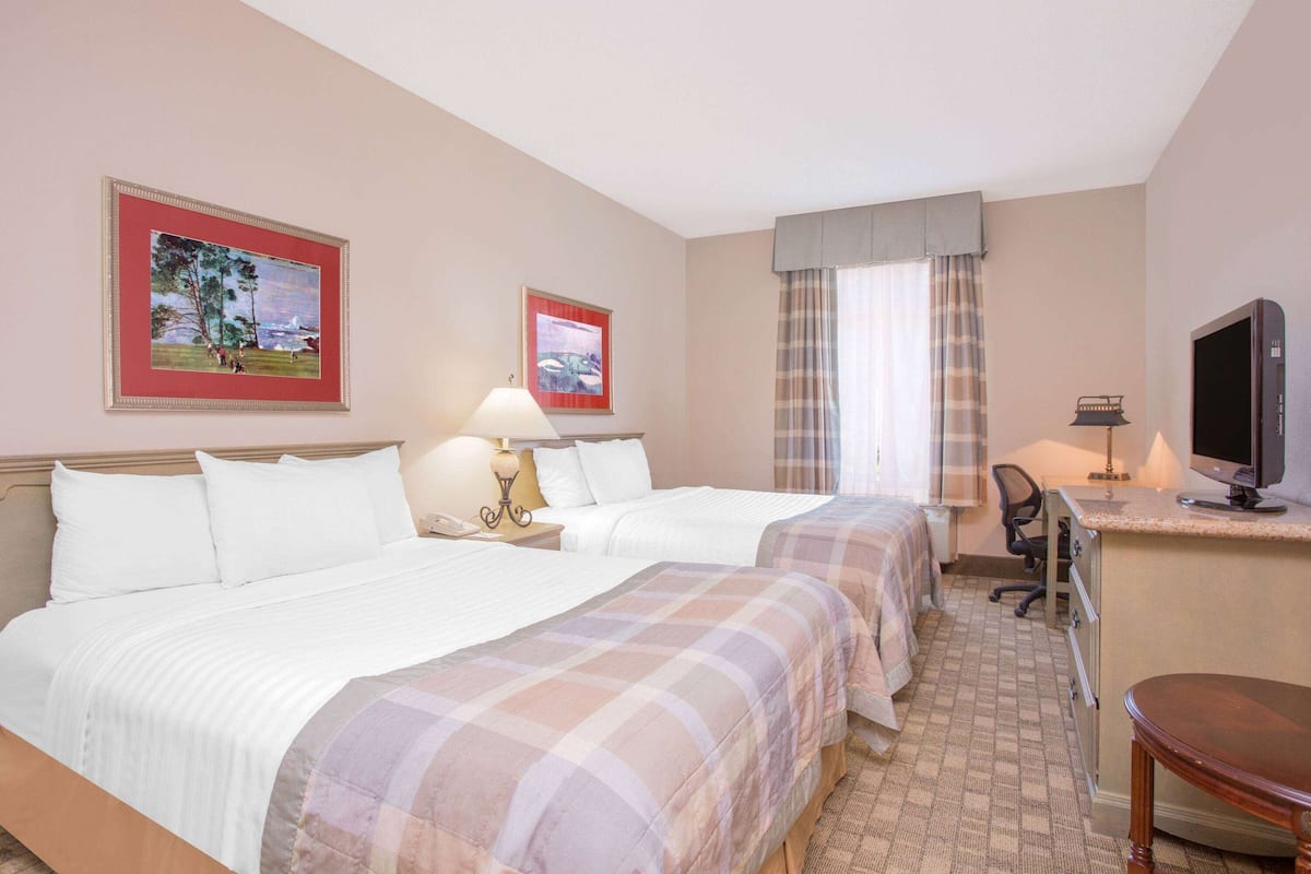 Quarto de hotel com duas camas, uma escrivaninha, televisão e obras de arte nas paredes.