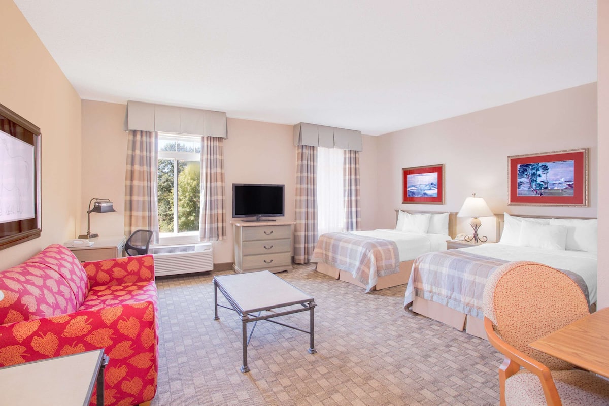 Quarto de hotel com duas camas, televisão, escrivaninha, cadeira e sofá.