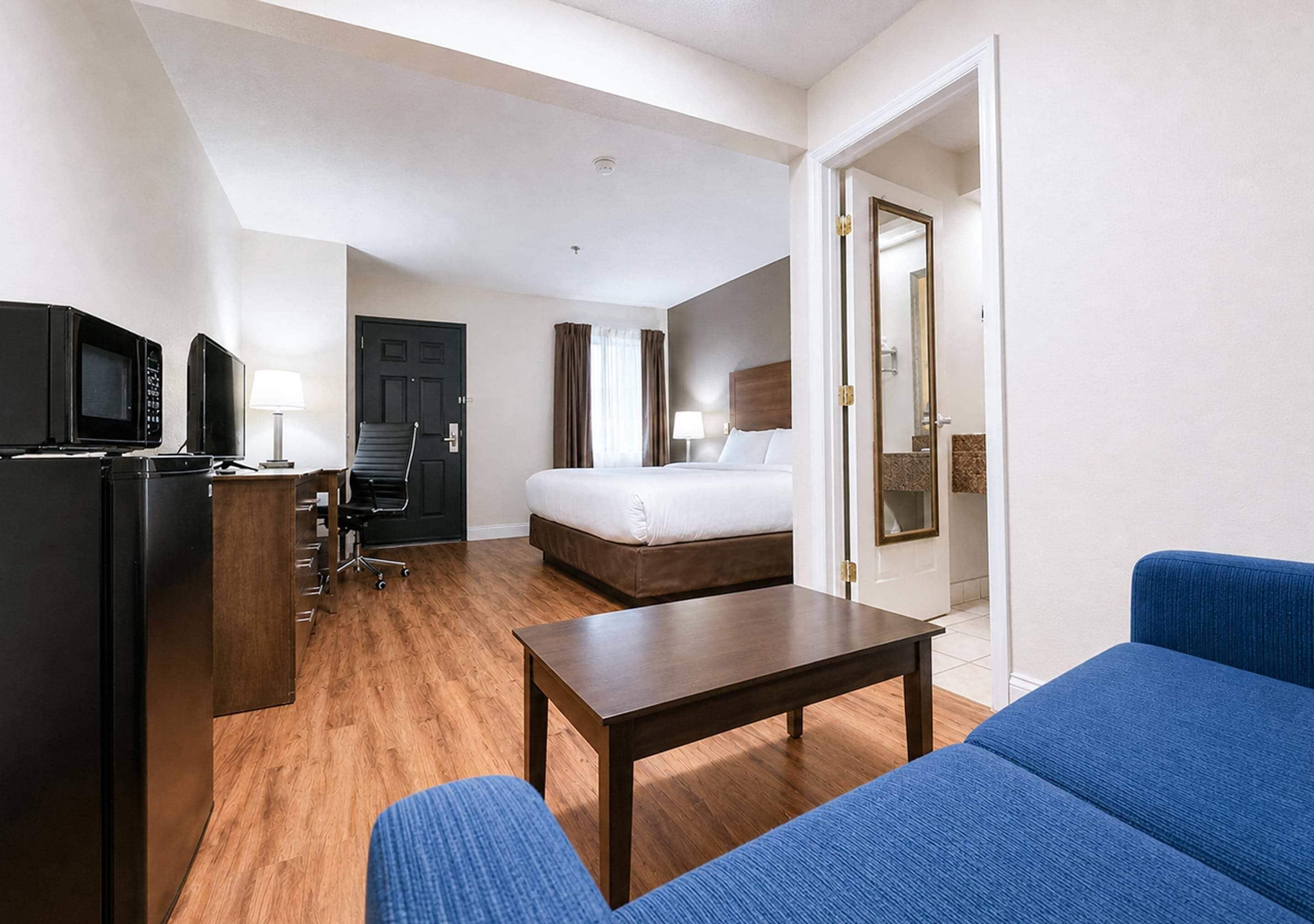 Quarto de hotel com cama, escrivaninha, cadeira, televisão e abajur.