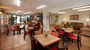 A hotel lobby with a dining area, a sofa, and a kitchen in the background. - Quality Inn Augusta West Near Fort Gordon (Augusta)