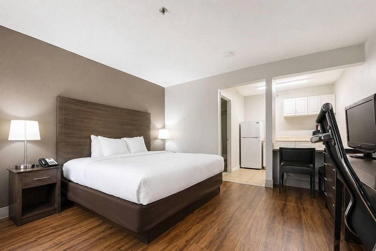 A hotel room with a bed, a desk, a chair, a TV, a lamp, and a phone on a nightstand.