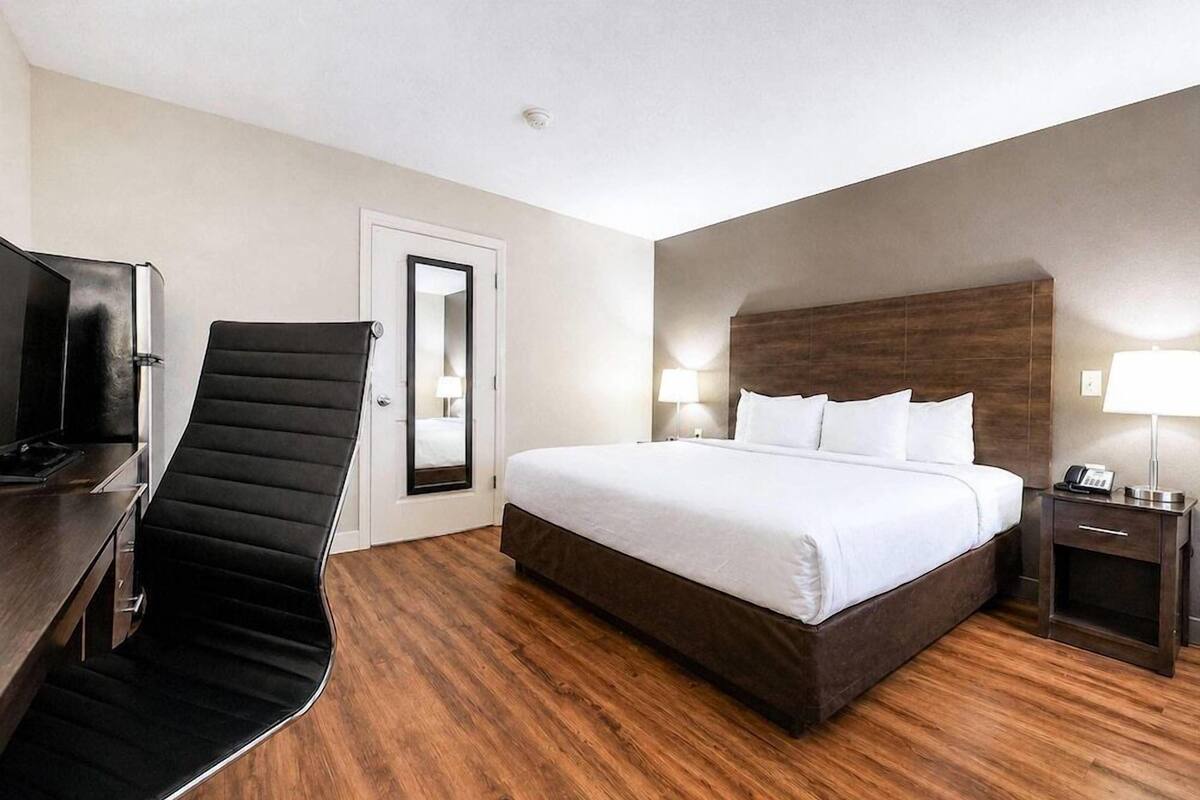 A hotel room with a bed, a desk with a chair, a TV, a nightstand, and a door.