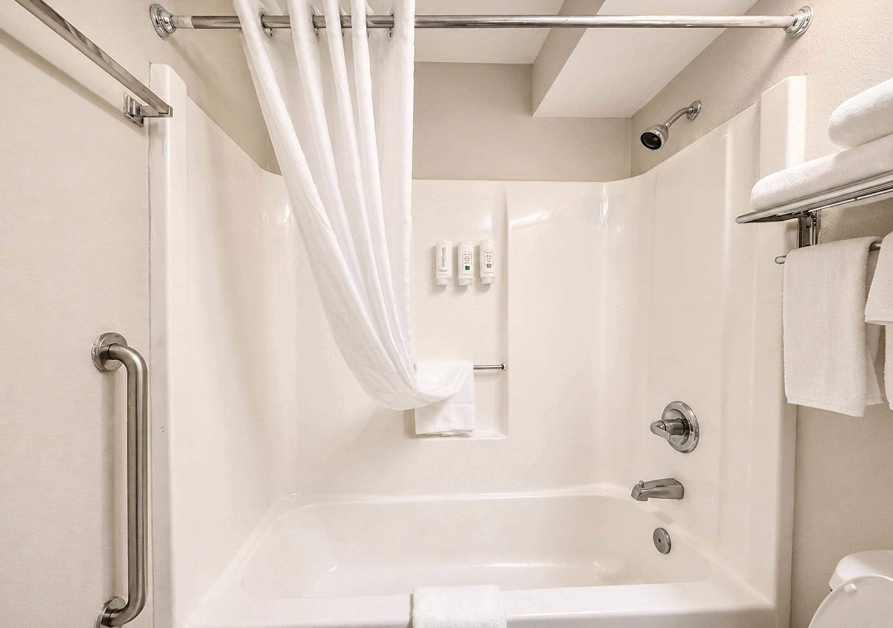 A modern bathroom with a bathtub, a shower curtain, a towel rack, and a handrail.