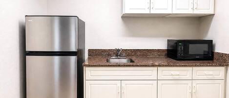 Una cocina con refrigerador de acero inoxidable, microondas y gabinetes blancos.