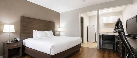 Habitación de hotel con cama, mesitas de noche, escritorio, silla, televisor y kitchenette.