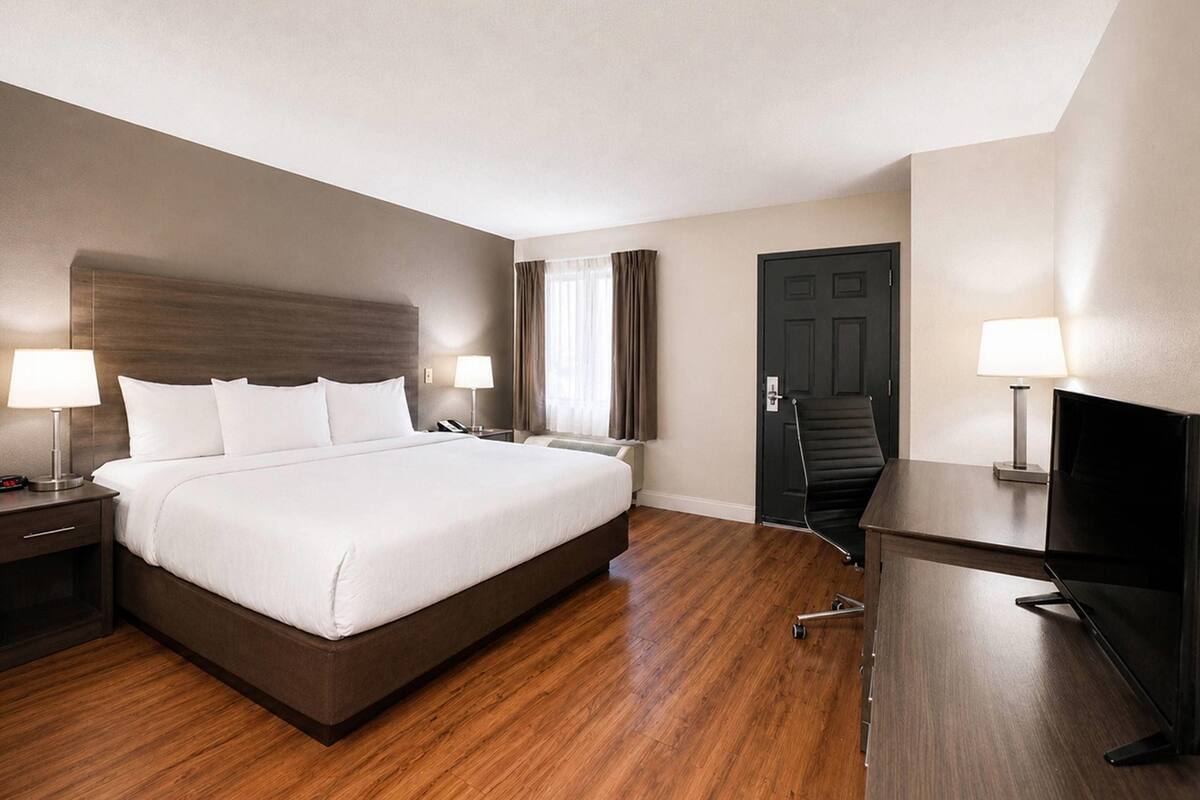 A hotel room with a large bed, bedside tables with lamps, a desk with a television, and a door.