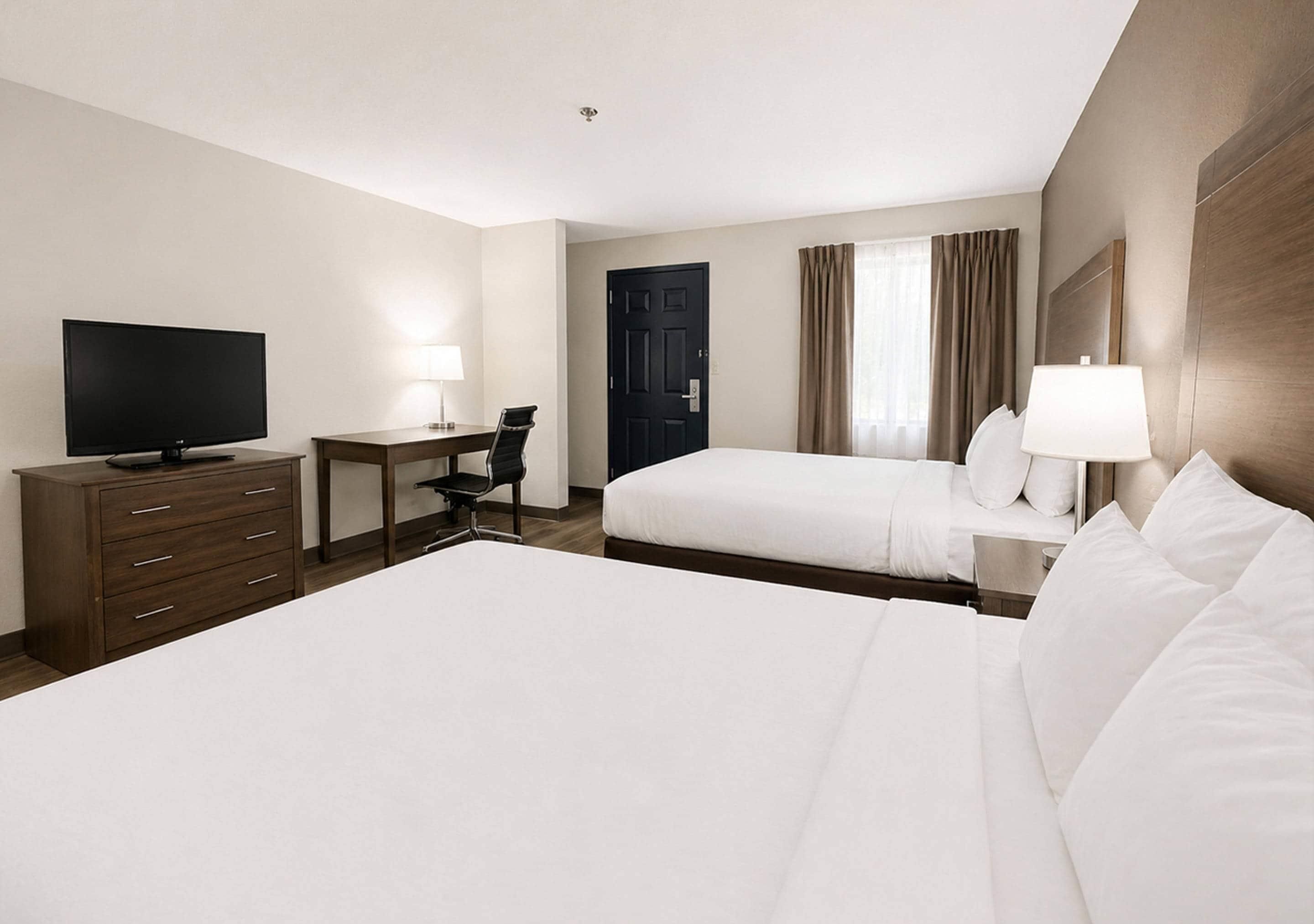 Une chambre d’hôtel avec un grand lit, un bureau avec une chaise, une télévision et une porte.