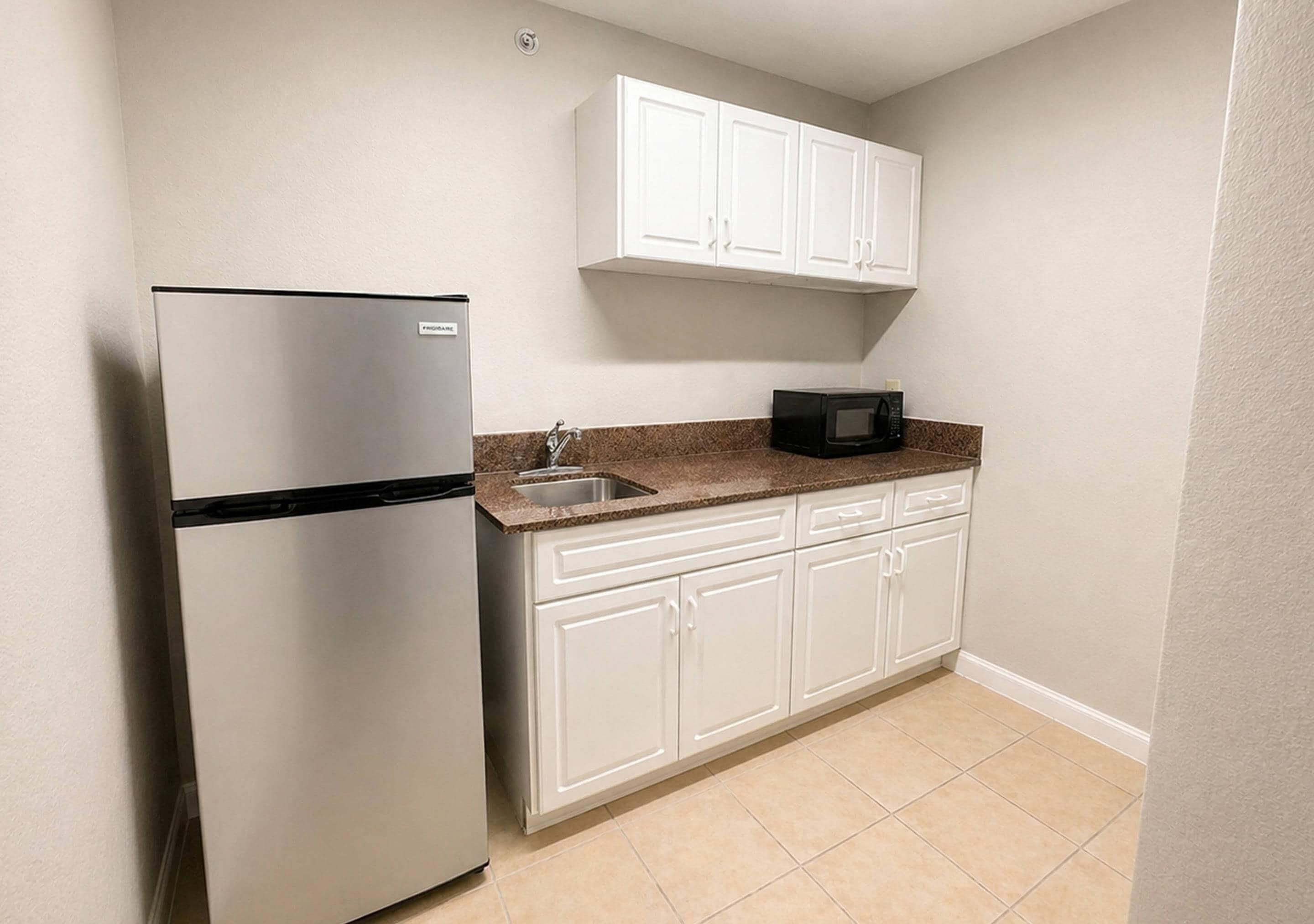A compact kitchen with white cabinets, a stainless steel refrigerator, a microwave, and a sink.