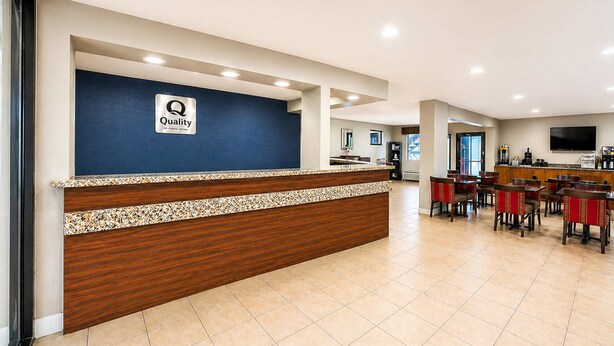 A hotel reception area with a blue wall, a wooden reception desk, and a tiled floor. - Quality Inn Augusta West Near Fort Gordon (Augusta)