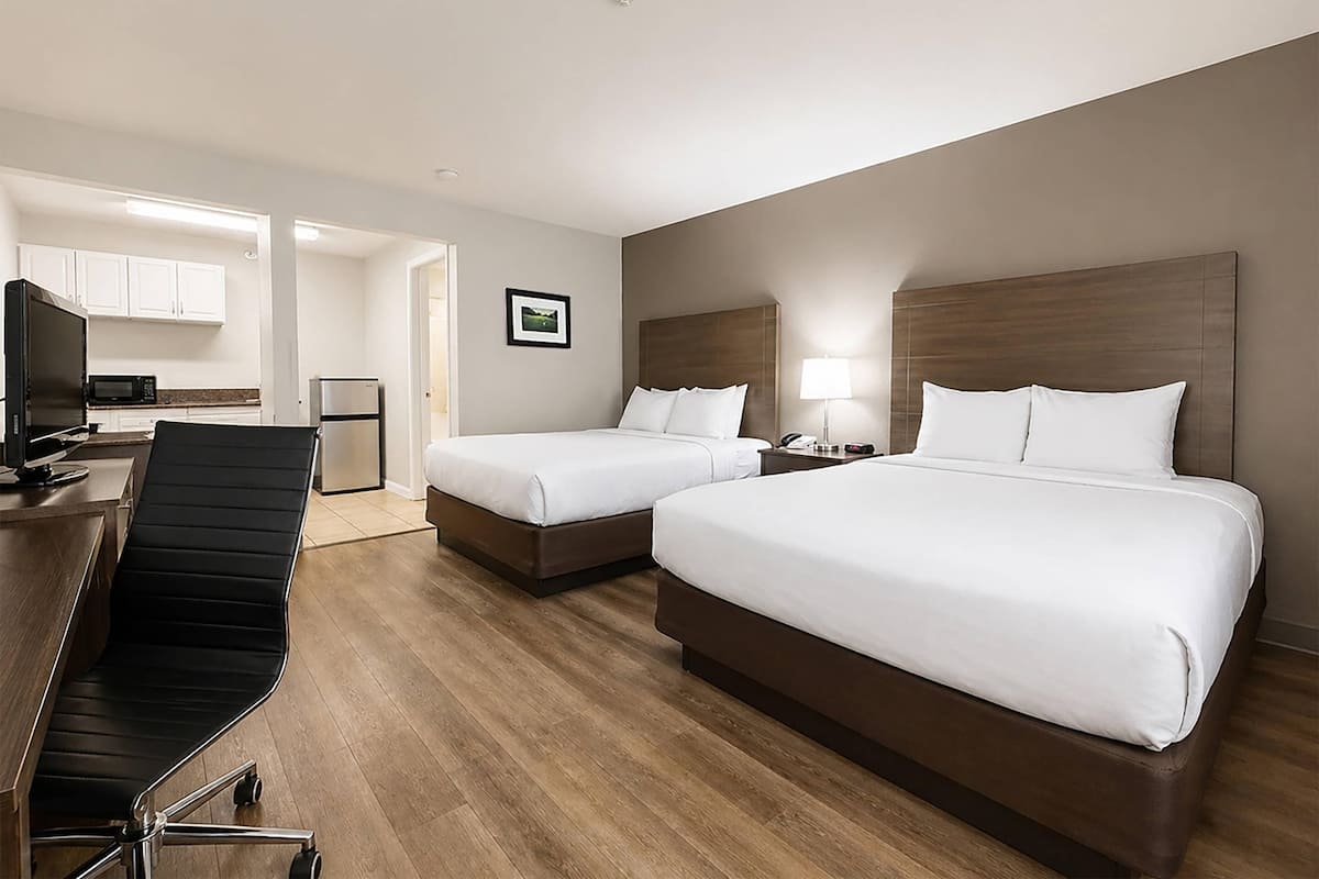 A hotel room with two beds, a desk with a chair, a microwave, and a refrigerator.