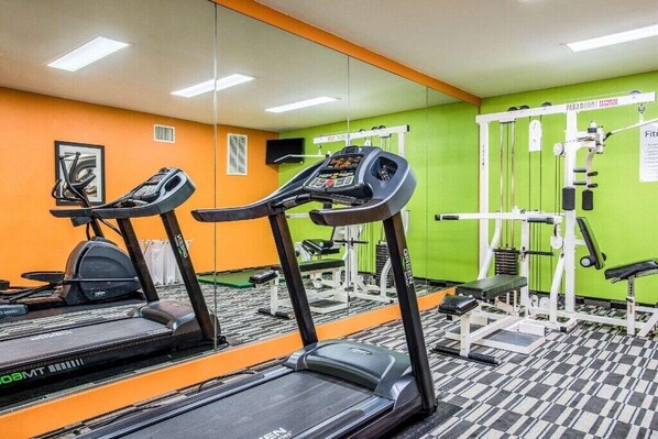 A gym with treadmills, weight machines, and a mirrored wall.