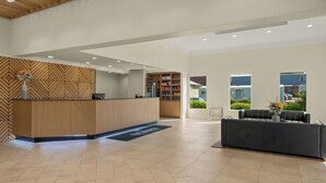 A modern reception area with a wooden reception desk, a black sofa, and a bookshelf. - The Marco Hotel Lake Charles (Lake Charles)
