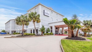 A modern hotel with a white facade, palm trees, and a clear blue sky. - The Marco Hotel Lake Charles (Lake Charles)