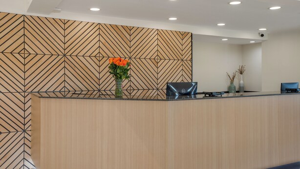 A reception desk with a geometric patterned wall, a vase with orange flowers, and a computer monitor.