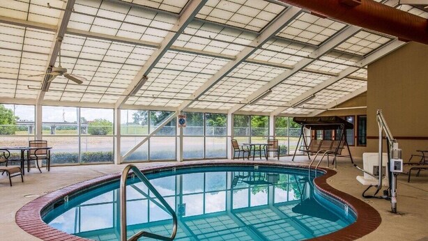 An indoor swimming pool with a glass enclosure, surrounded by lounge chairs and tables. - The Marco Hotel Lake Charles (Lake Charles)