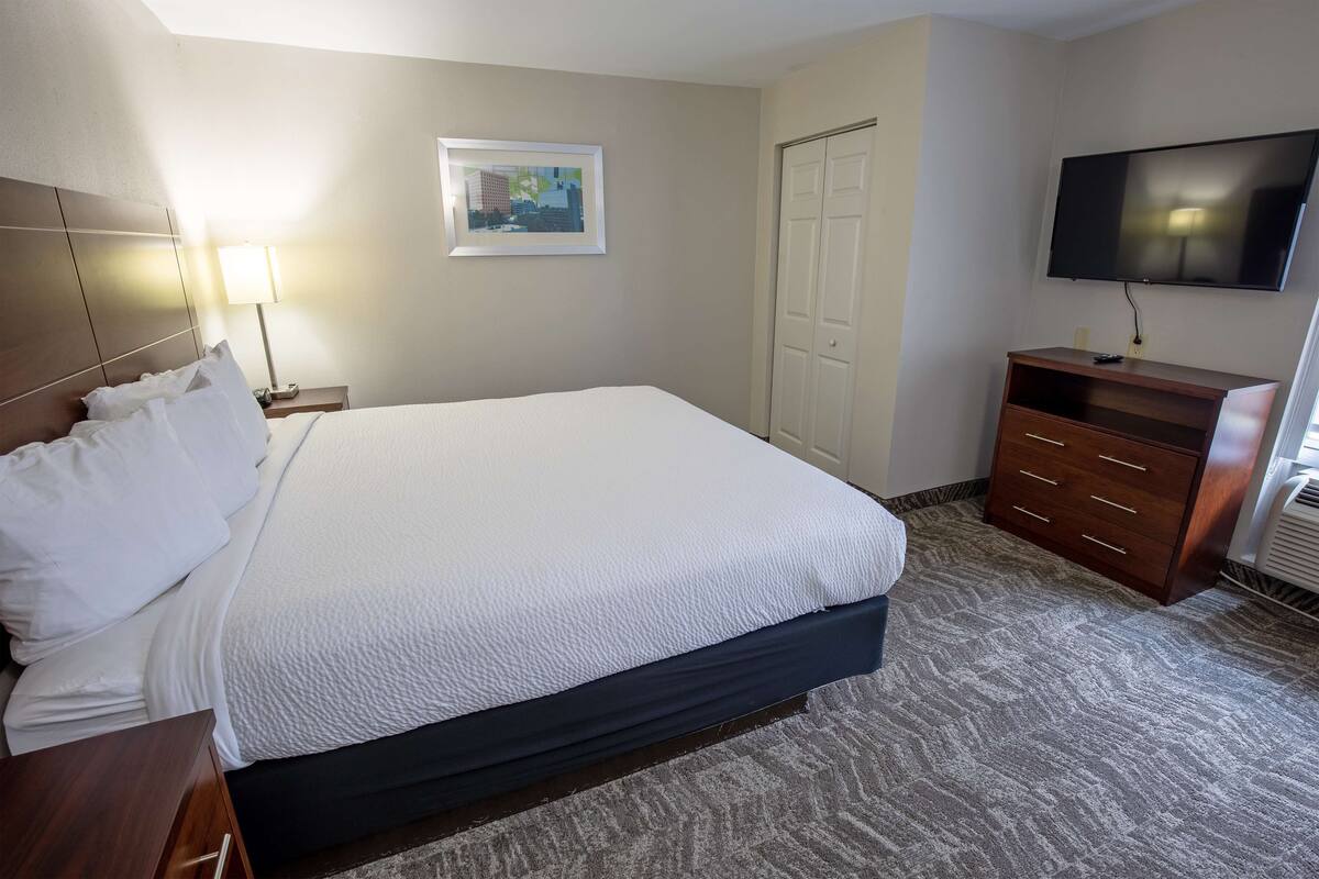 A hotel room with a large bed, a nightstand, a dresser, a television, and a framed picture on the wall.