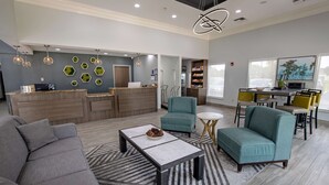 A modern lobby with a reception desk, seating area, and a dining setup.
