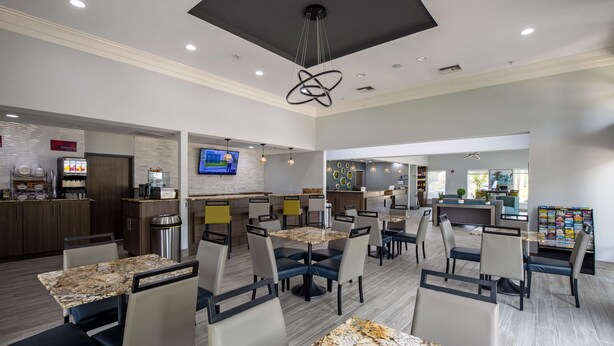 A modern hotel lobby with a central seating area, a kitchen counter, and a television mounted on the wall.