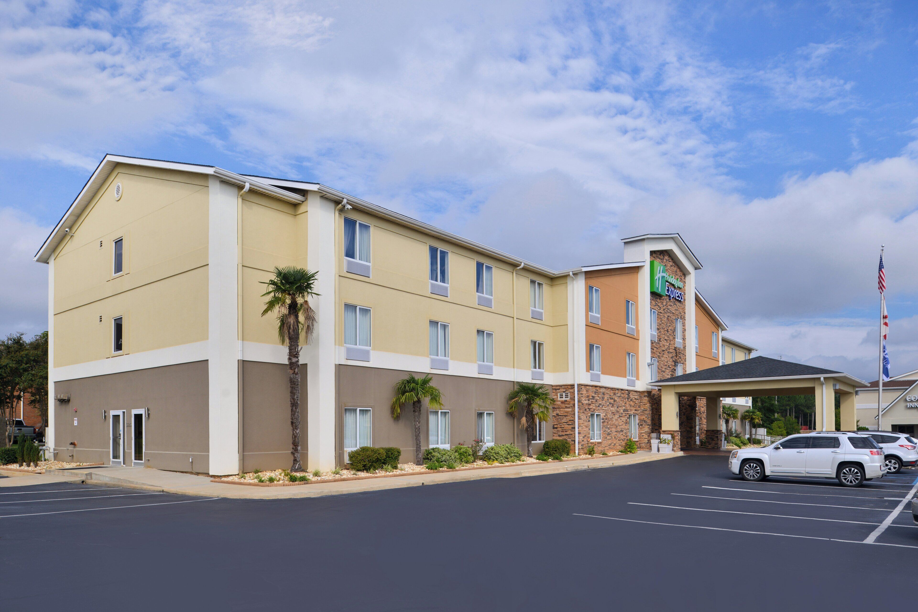 Um hotel de vários andares com telhado plano, placa Holiday Inn Express e estacionamento com vários carros.