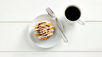 Ein weißer Teller mit Gebäck und einer Gabel, dazu eine Tasse schwarzer Kaffee auf einer weißen Holzoberfläche.
