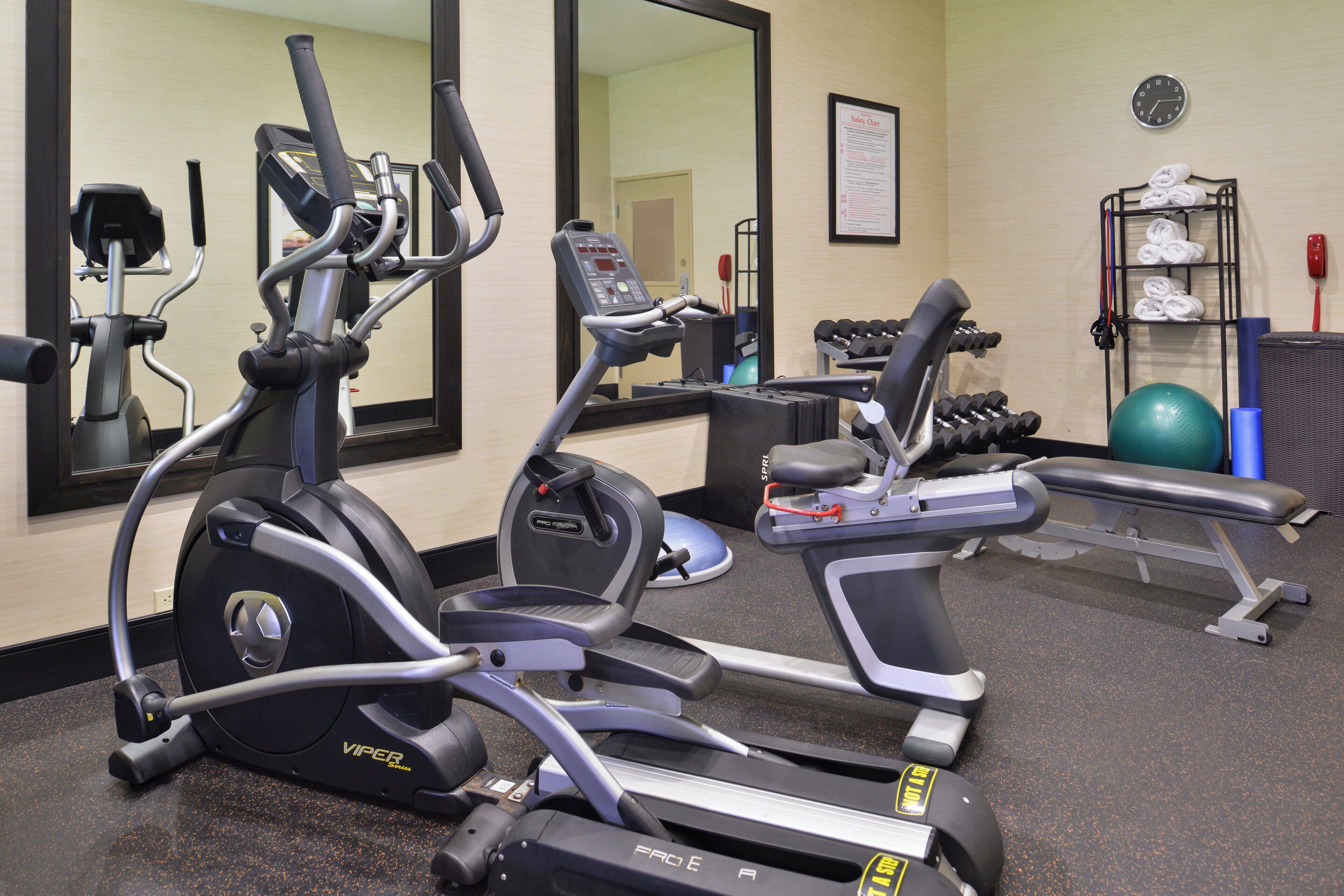 A gym with various exercise equipment including treadmills, a bench, and dumbbells.