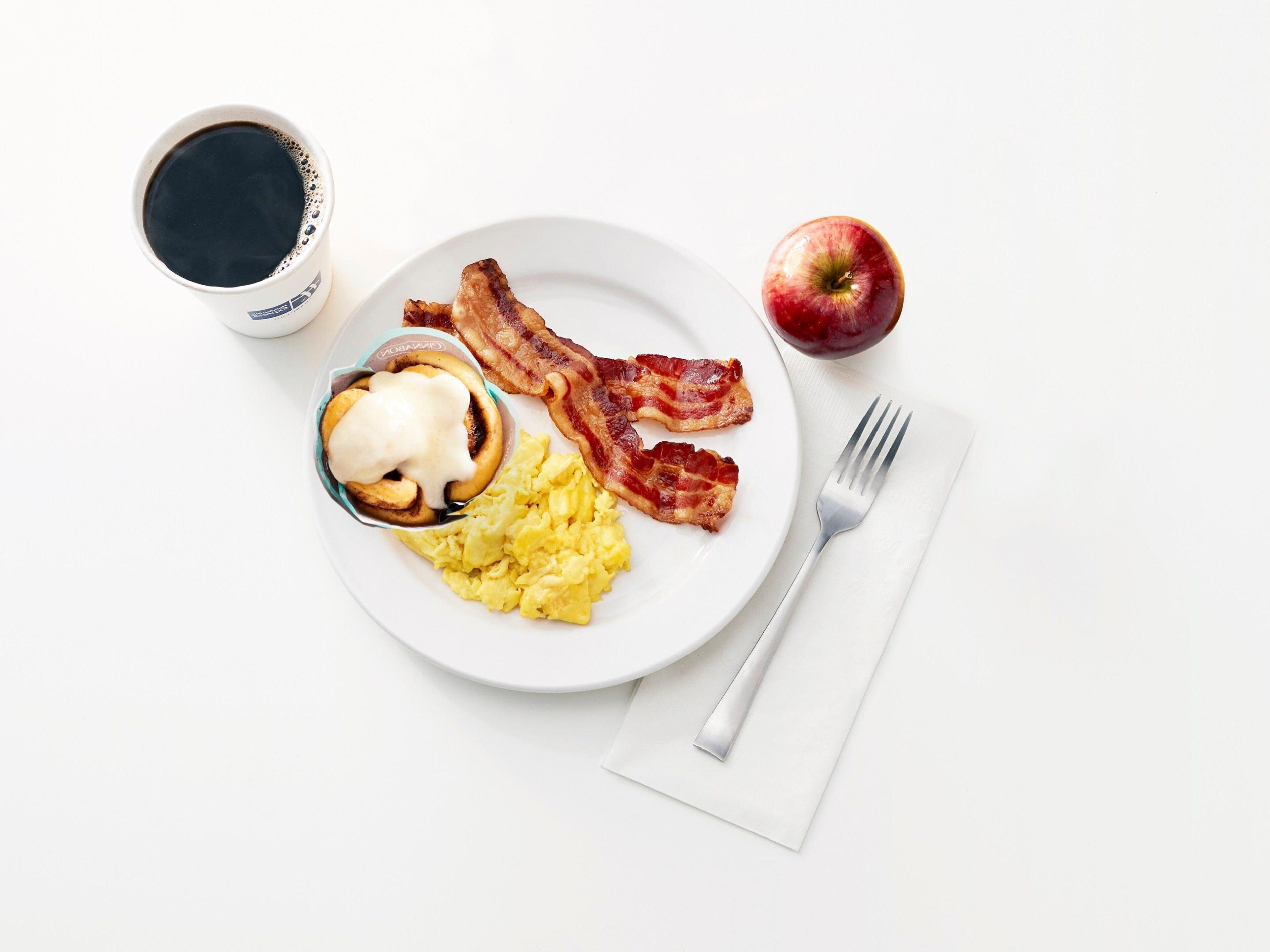 A plate with scrambled eggs, bacon, a poached egg, and a cup of coffee on a white table.