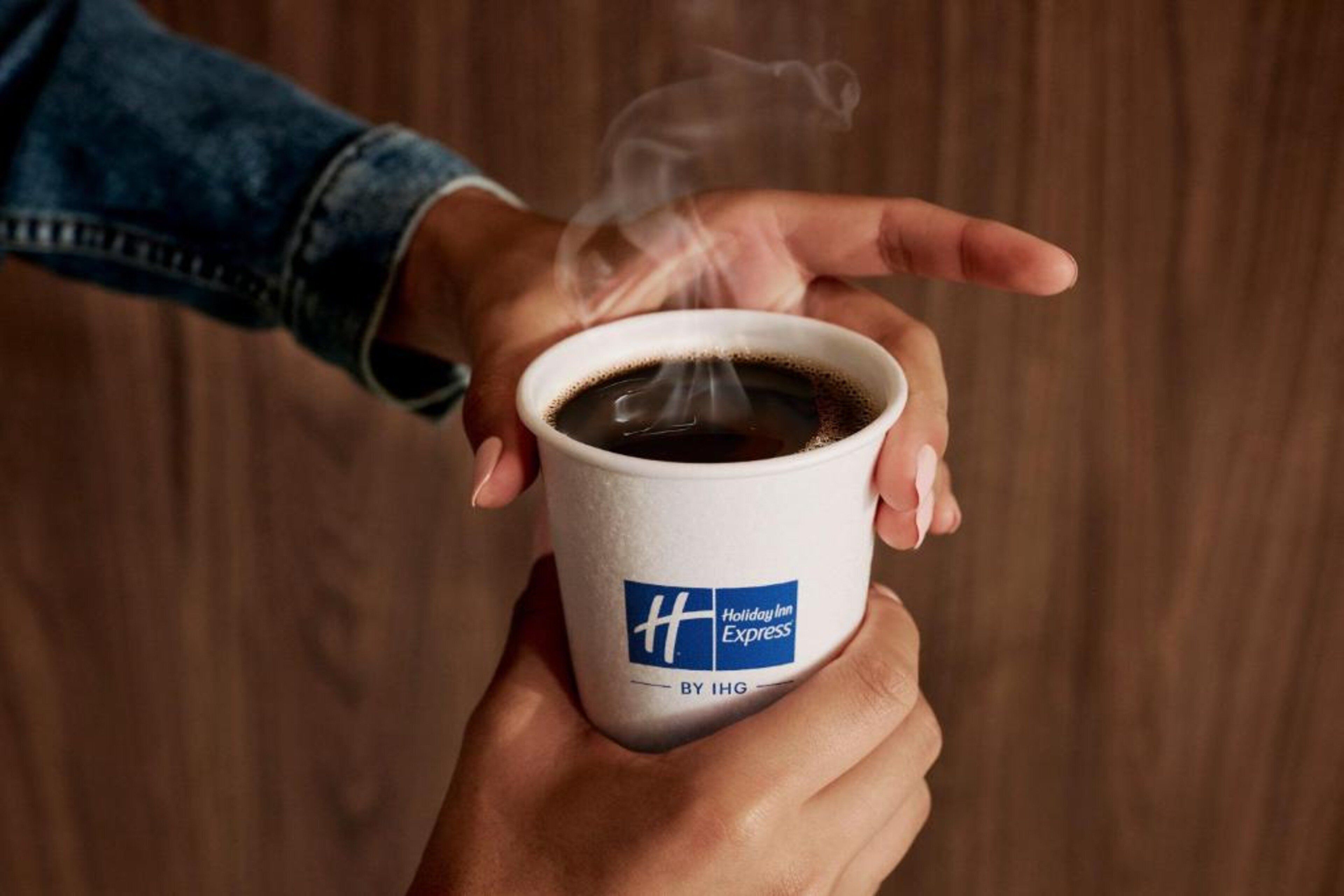 A hand holding a cup of coffee with steam, featuring the Holiday Inn Express logo.