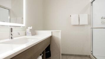 A modern bathroom with a large mirror, two sinks, a towel rack, and a shower area.