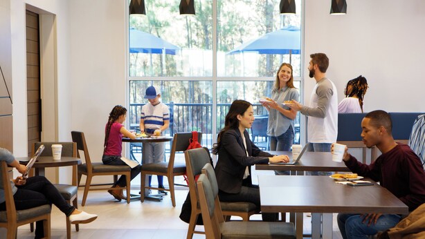 A modern indoor space with tables and chairs, large windows, and pendant lighting.