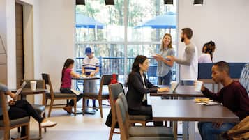 A modern indoor space with tables and chairs, large windows, and pendant lighting.