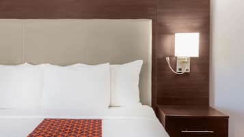 Quarto de hotel com uma cama grande, uma mesinha de cabeceira e um criado-mudo.