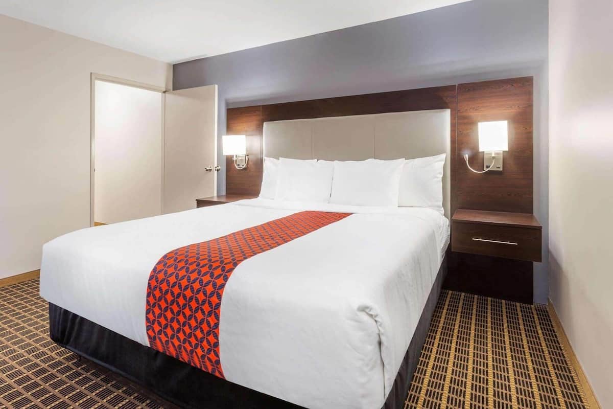 Una habitación de hotel con una cama grande, una mesita de noche, una lámpara de pared y una puerta.