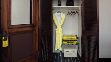 A hotel room with a wooden door, a robe hanging on a rack, a suitcase, and a small table with a device.
